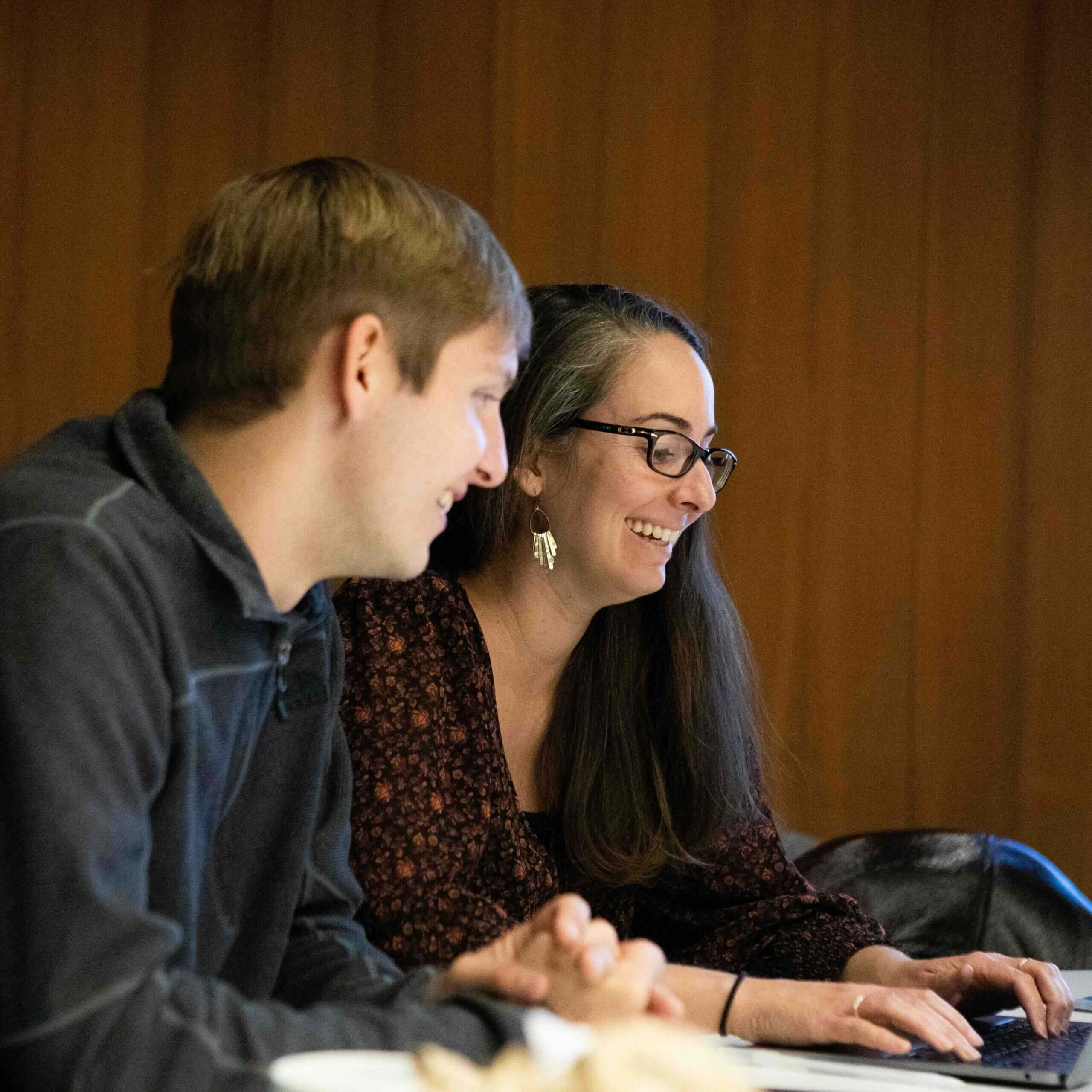 Two people working together on a laptop at a table.