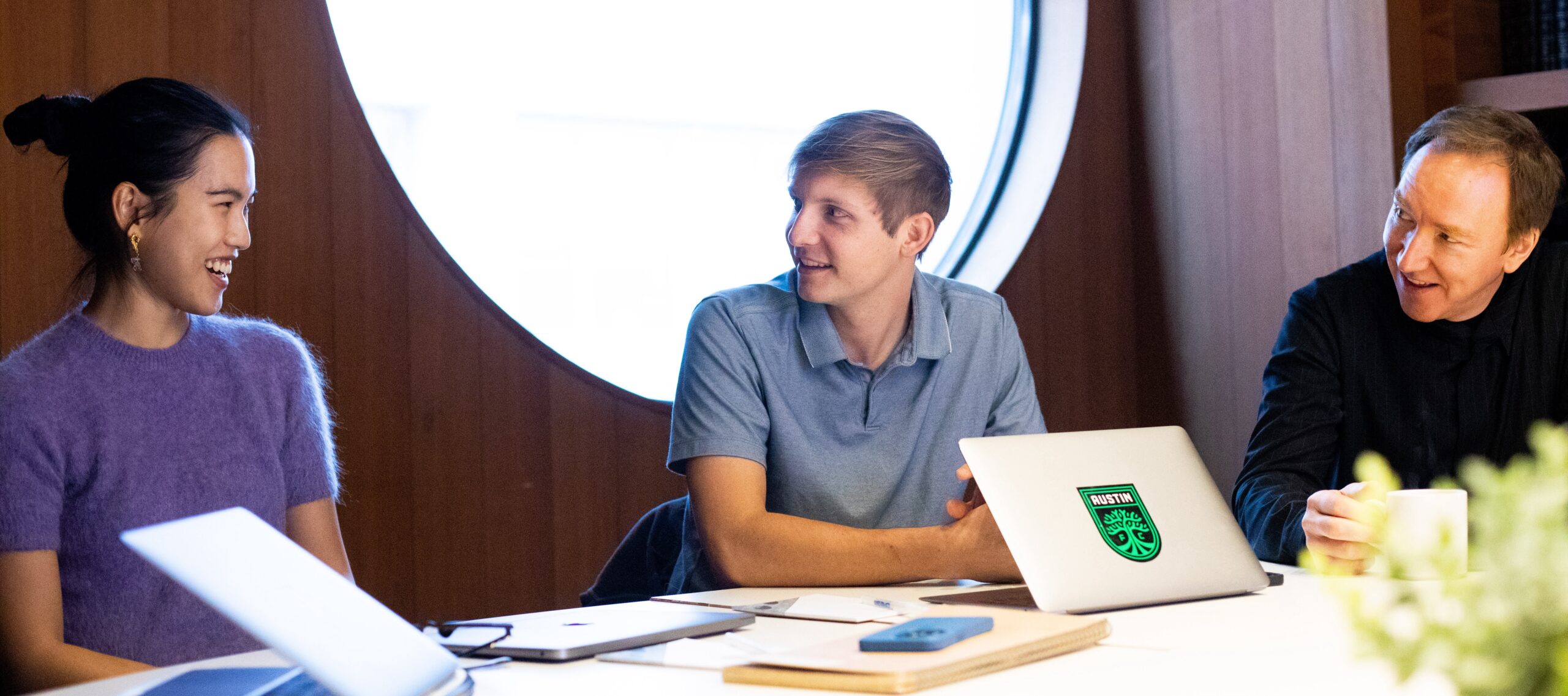 Three people sitting at a table with laptops smiling